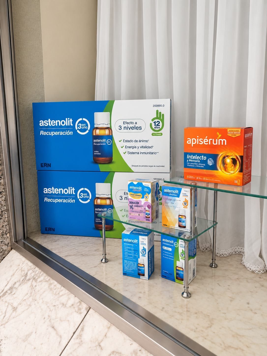 Varias cajas de medicamentos y suplementos expuestas sobre una mesa de cristal, junto a una cortina y un suelo de baldosas.