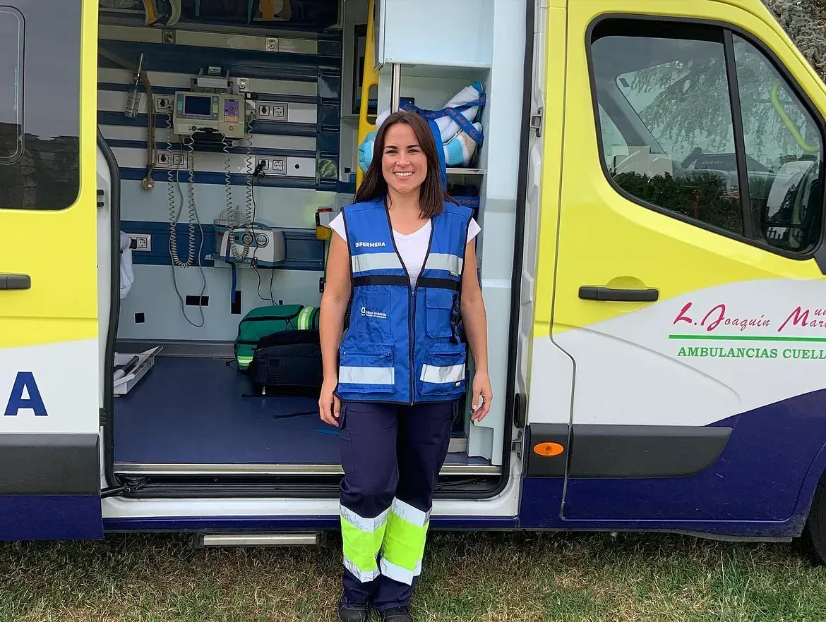 Una mujer está parada frente a una ambulancia con la puerta abierta.