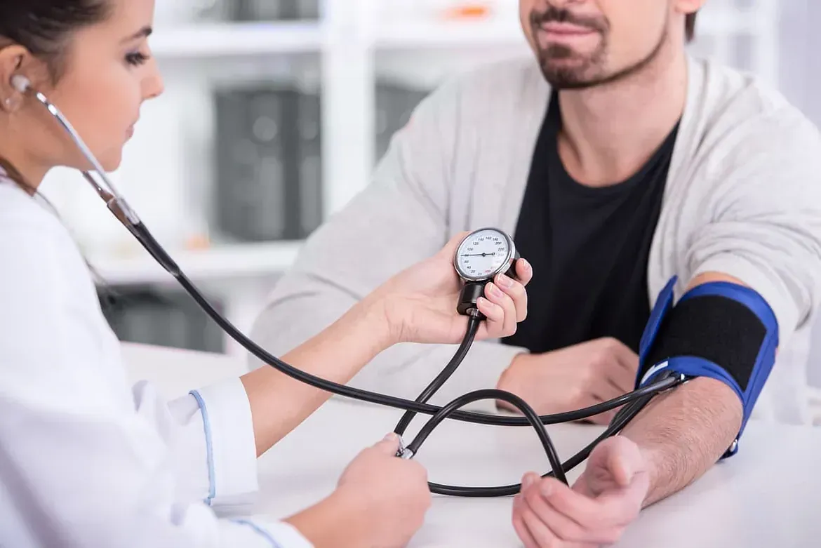 mujer médico tomando la presión arterial con un tensiométro de un hombre joven con barba