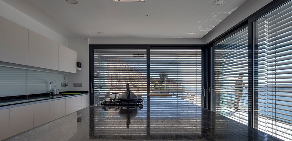 Intérieur d'une cuisine moderne blanche entourée de baie vitrée et brise soleil par dessus