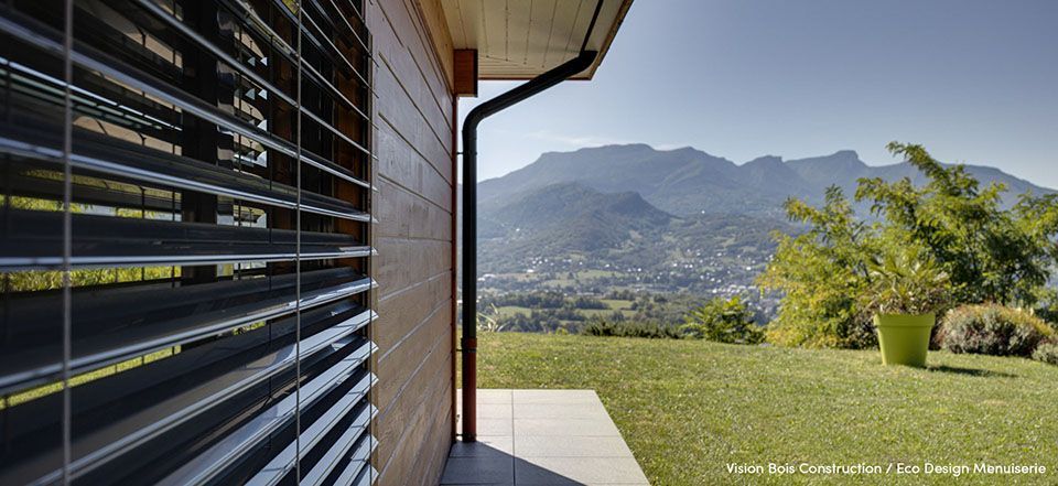 Belle vue sur un paysage de montagne avec façade de maison et brise-soleil en aluminium noir sur façade bois