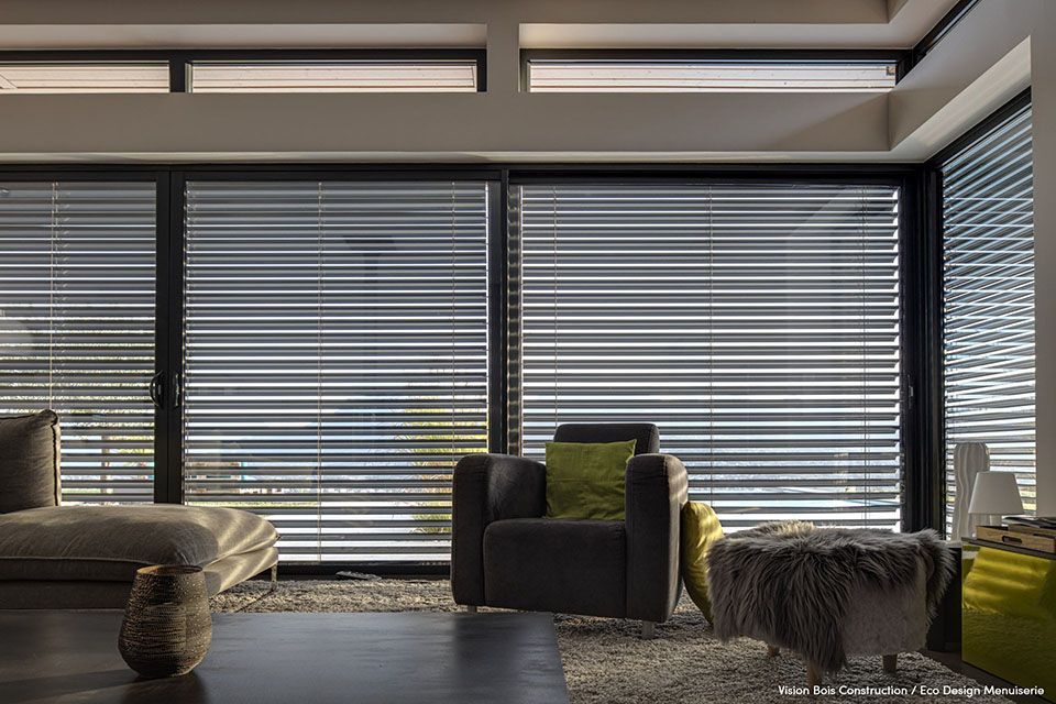 Vue intérieure d'un salon avec grande baie vitrée et menuiserie noire