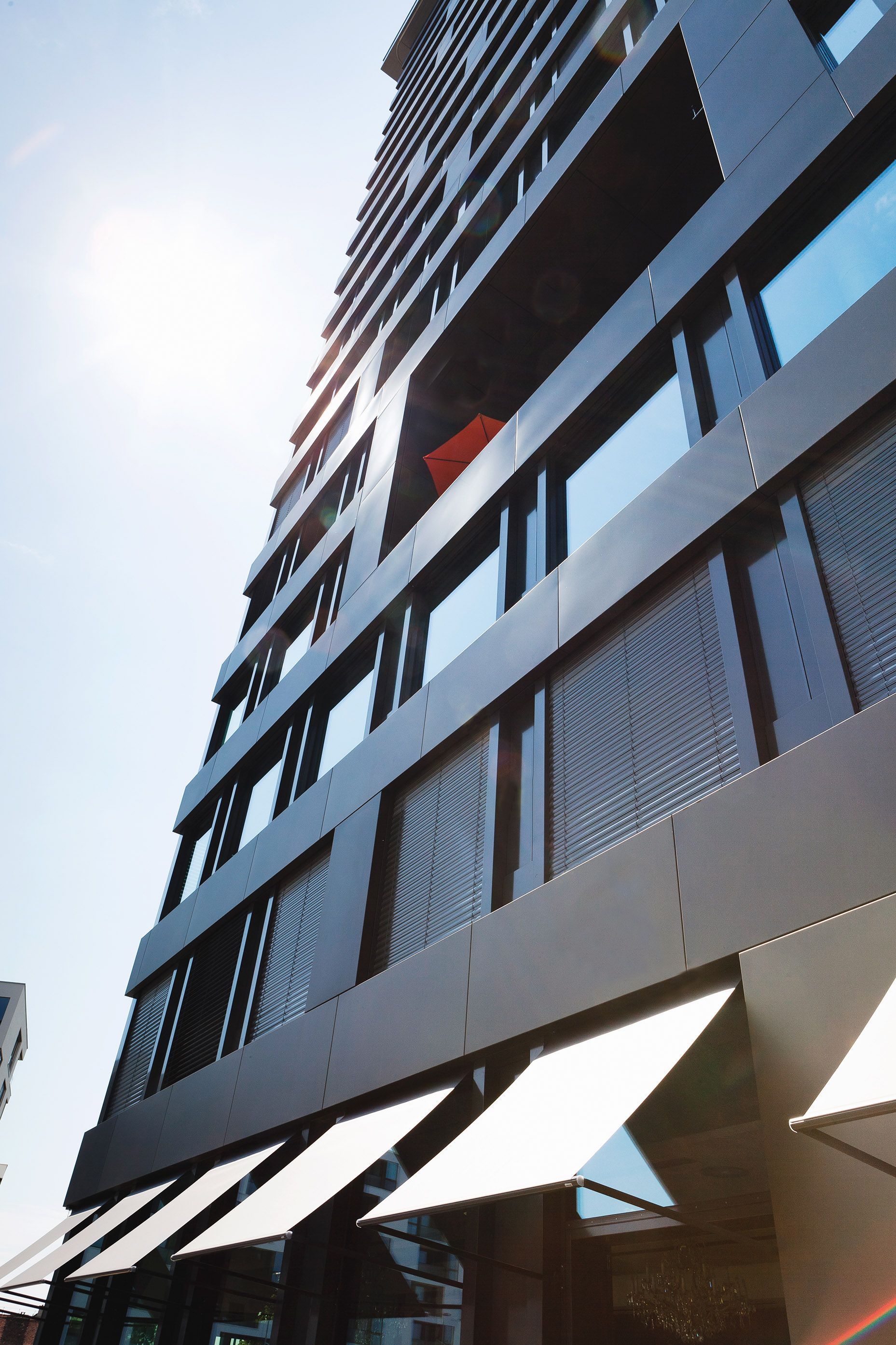 Façade d'un immeuble noir avec brise-soleil et store en toile