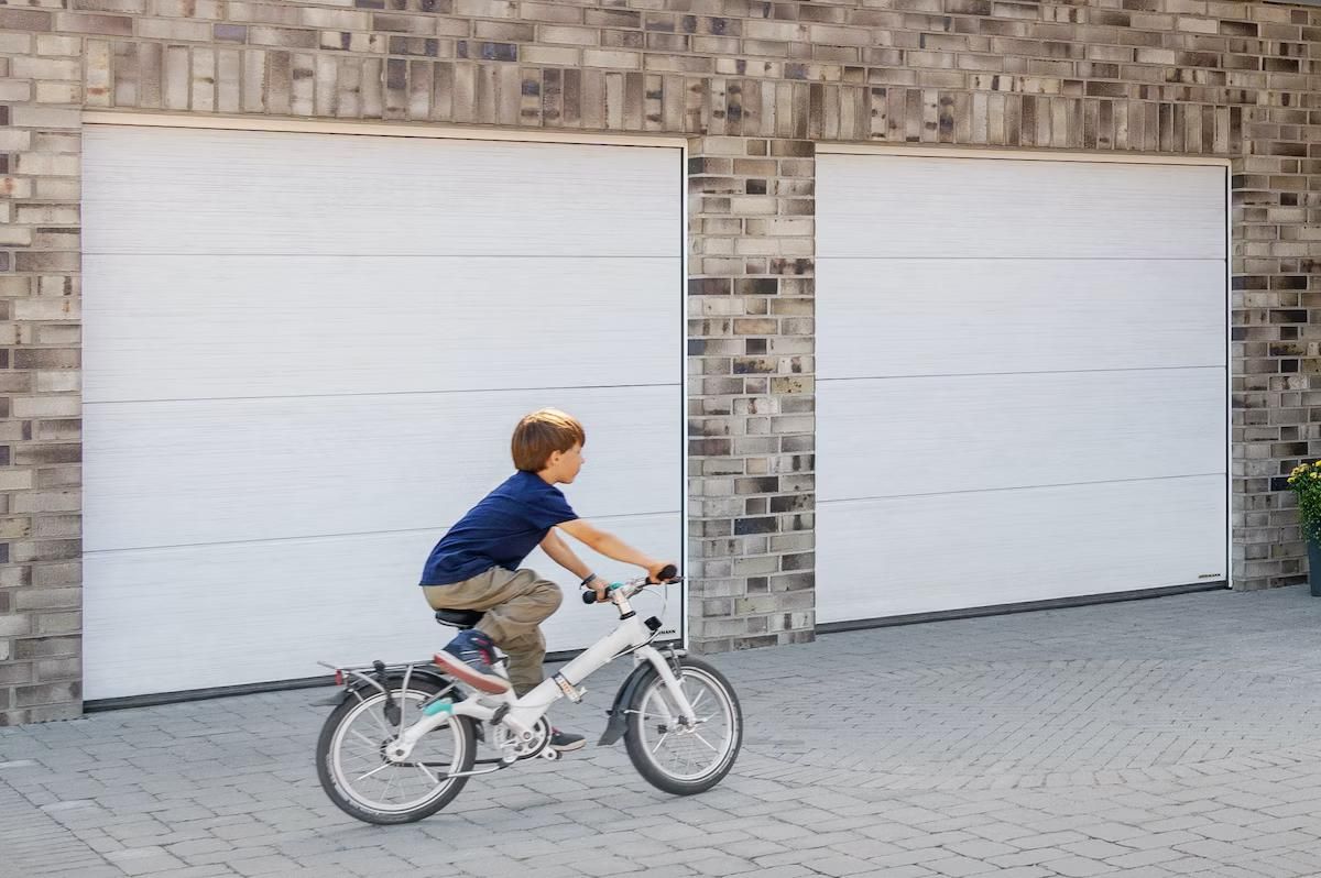double porte de garage blanche avec enfant en vélo passant devant