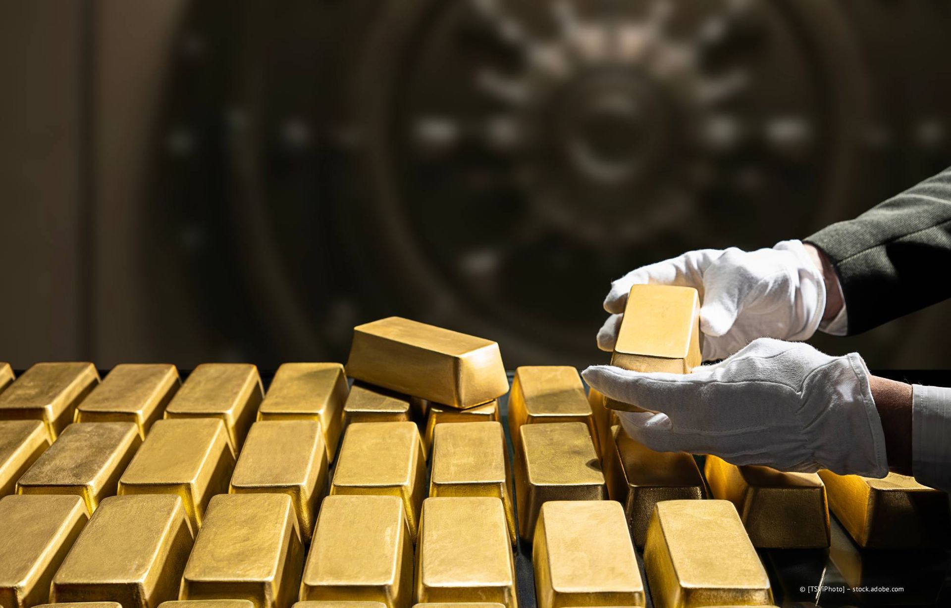 Hände in weißen Handschuhen stapeln Goldbarren in der Nähe einer Tresortür.