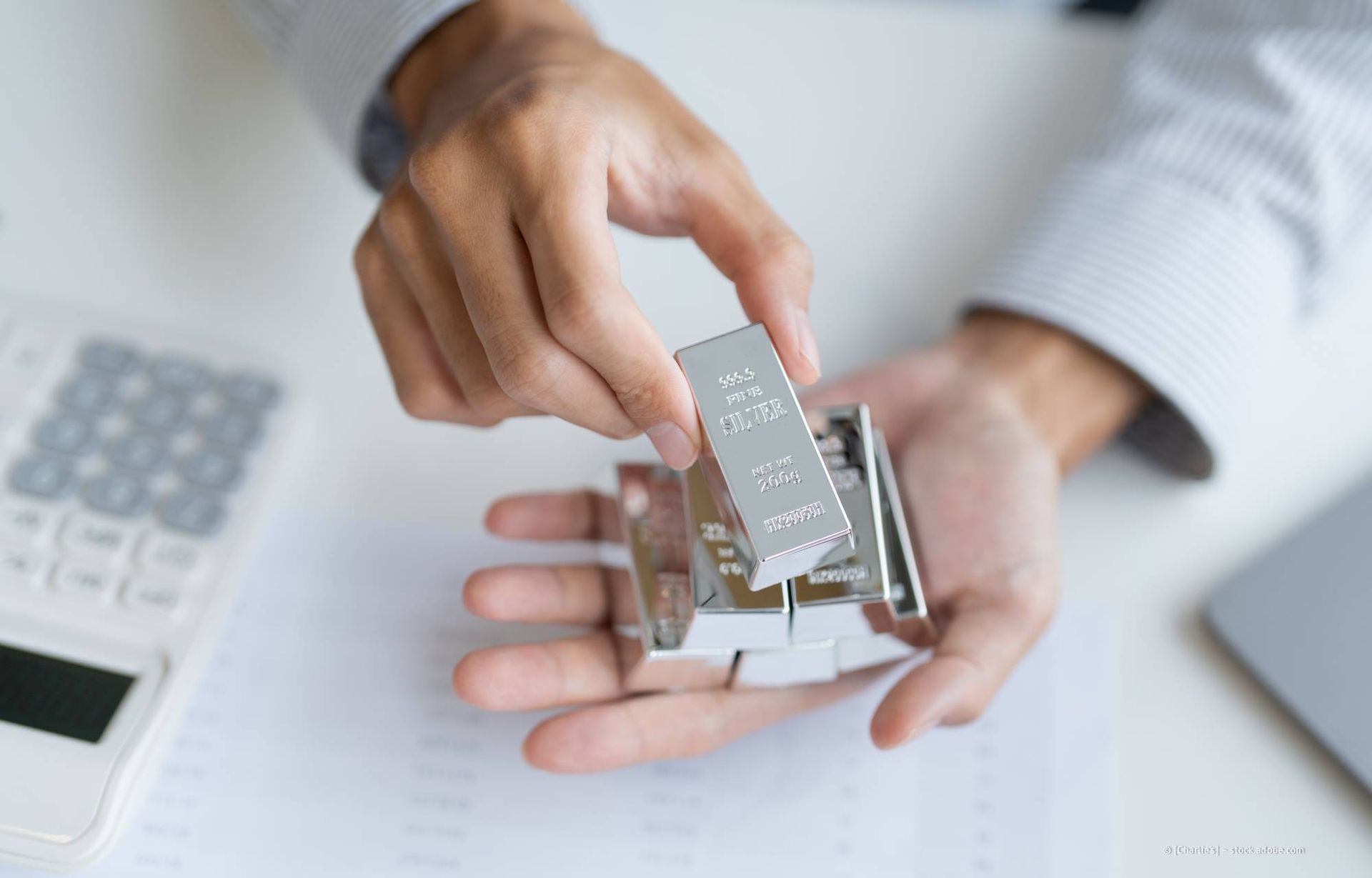 Eine Person hält mehrere Silberbarren in der Hand, möglicherweise in einem Büro.