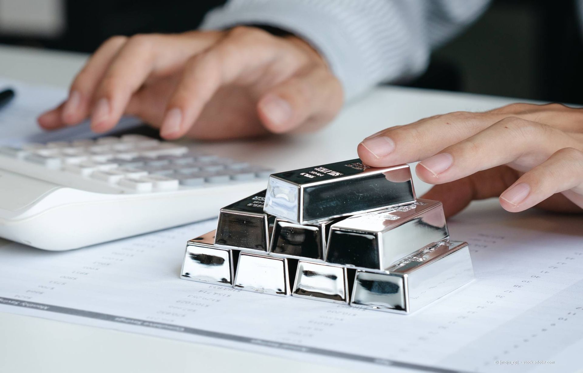 Eine Person rechnet mit einem Taschenrechner neben einem Stapel Silberbarren auf einem Dokument.