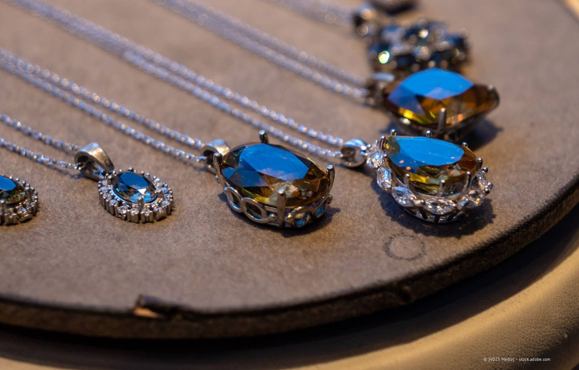 Nahaufnahme mehrerer türkisfarbener und silberner Halsketten, die auf einer grauen Fläche ausgestellt sind.