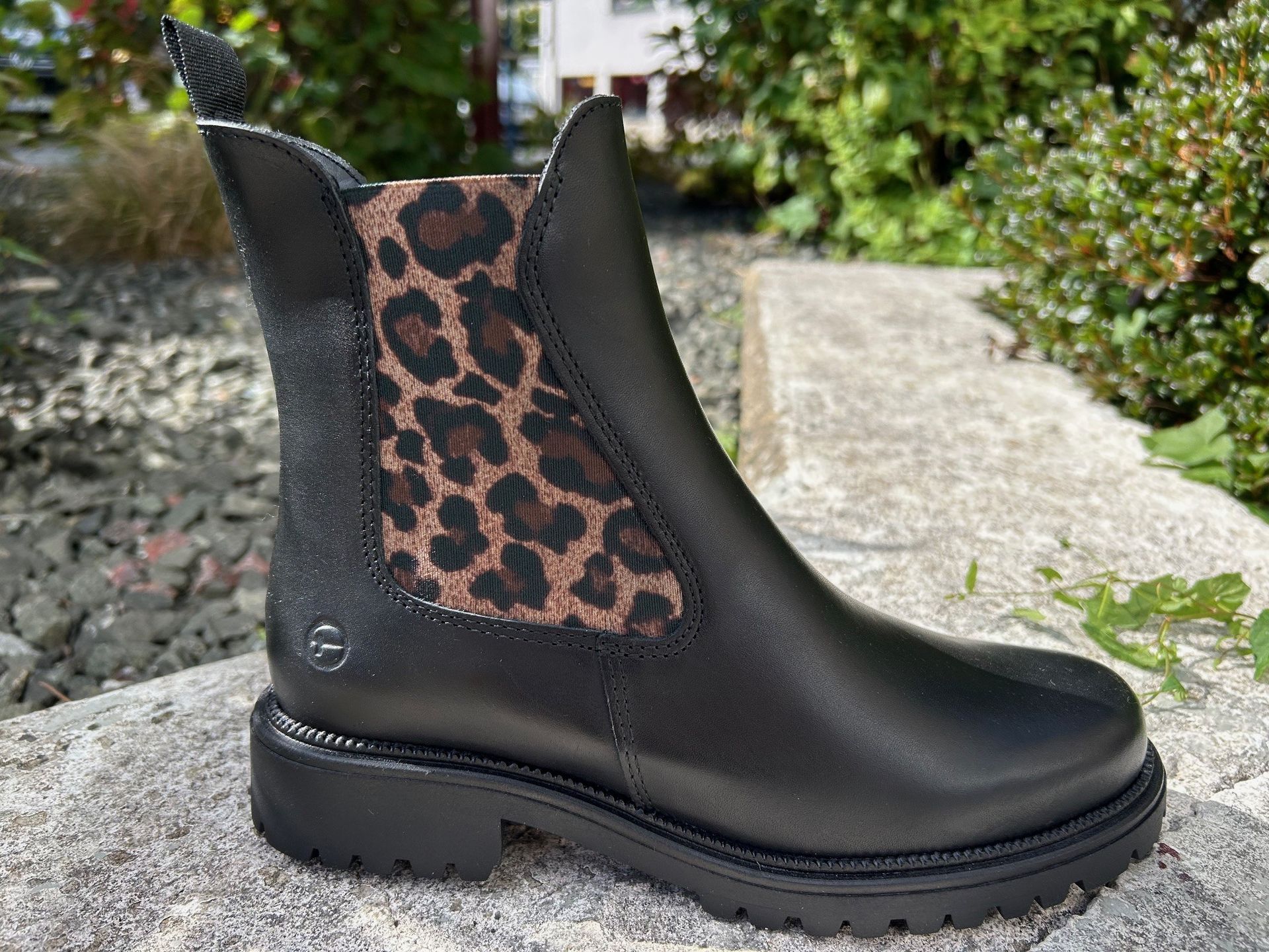 Schwarzer Tamaris Chelsea-Stiefel mit elastischem Einsatz im Leopardenmuster, im Freien auf Stein.