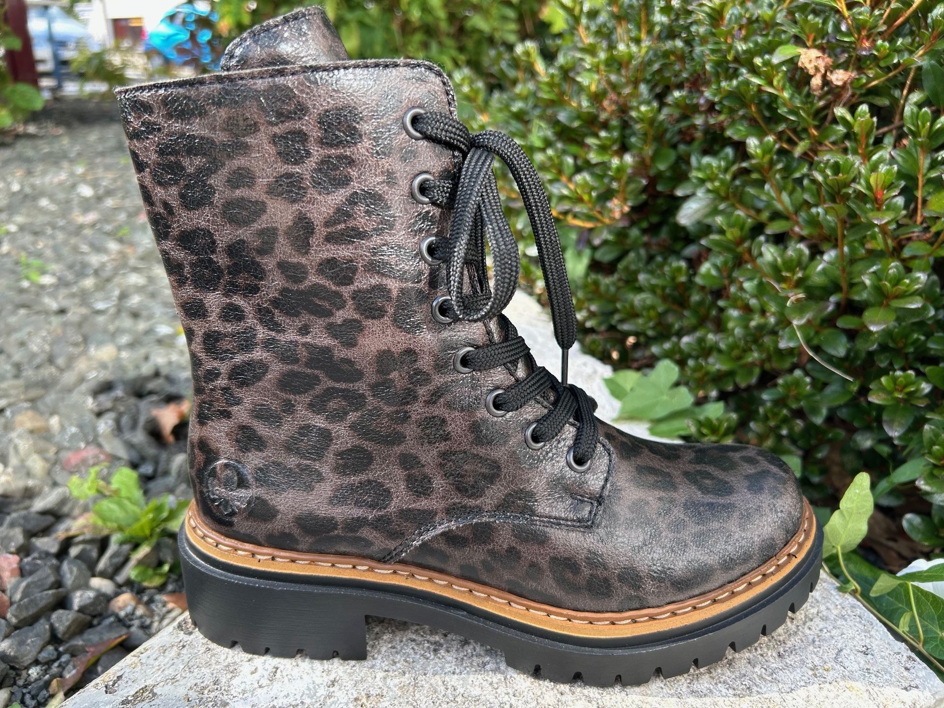 Stiefel mit Leopardenmuster, schwarzen Schnürsenkeln und braunem Besatz auf einem Stein.