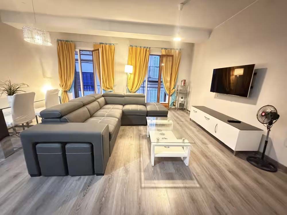 Sala de estar moderna con sofá seccional gris, televisor montado en la pared, consola blanca y cortinas amarillas.