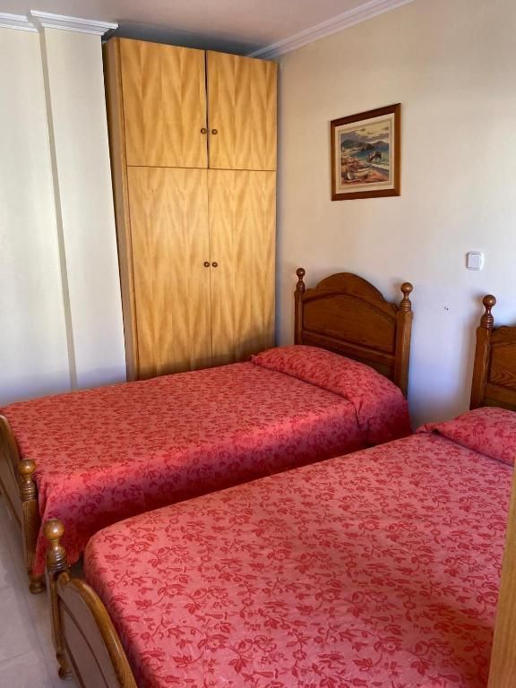 Habitación de hotel con dos camas individuales con fundas rojas, cabeceros de madera y un armario contra una pared color crema.