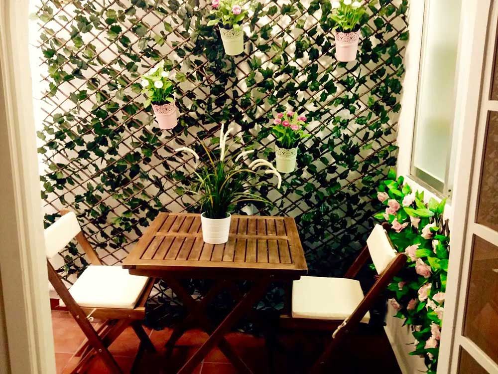 Pequeña zona de estar en el balcón con una mesa de madera, dos sillas y plantas en macetas sobre una celosía.