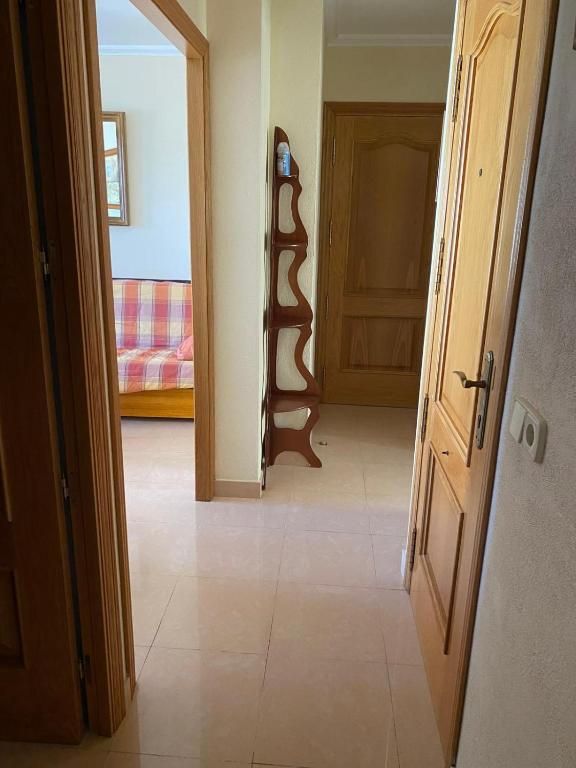 Pasillo estrecho con puertas de madera, suelo de baldosas y un dormitorio visible a través de una puerta abierta.
