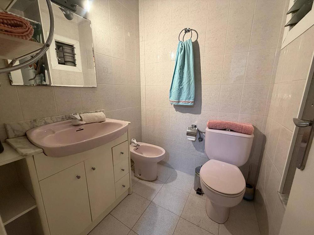 Baño pequeño con lavabo e inodoro rosas, suelo de baldosas blancas y una toalla azul colgada en la pared.