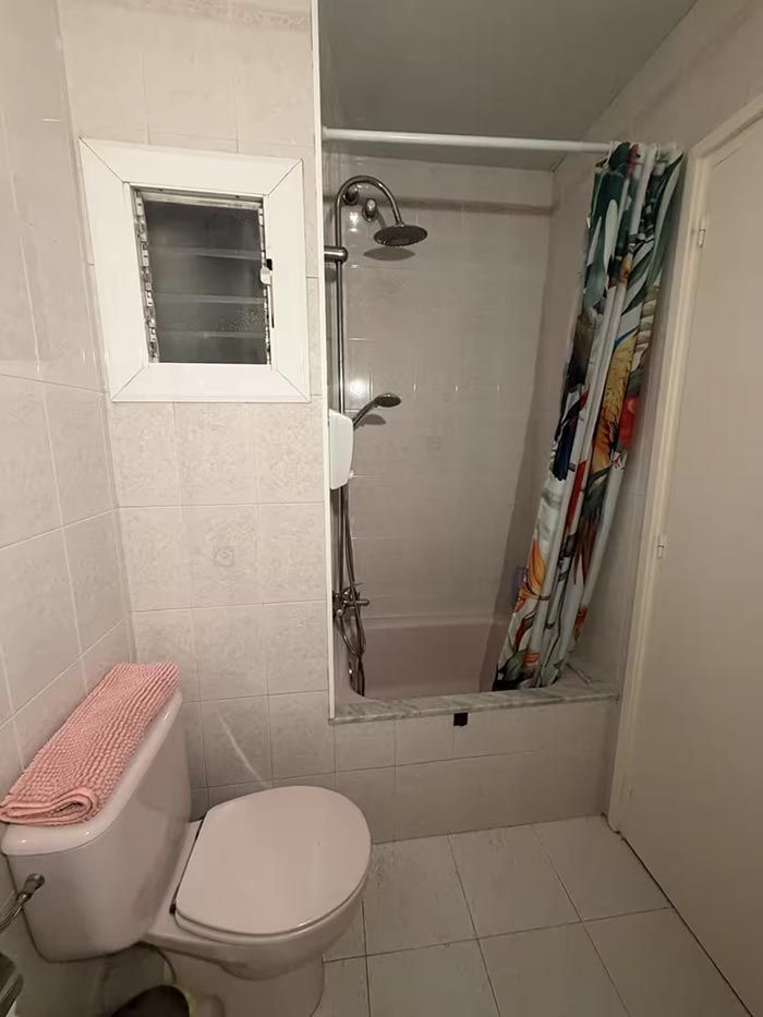 Baño pequeño con azulejos, inodoro, tapa de asiento rosa y cabina de ducha con cortina y puerta de cristal.