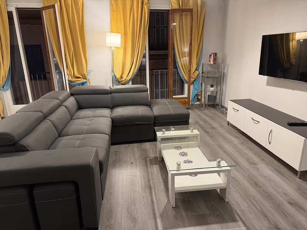 Sala de estar moderna con sofá seccional gris, televisor montado en la pared, mueble multimedia blanco y mesas de centro.