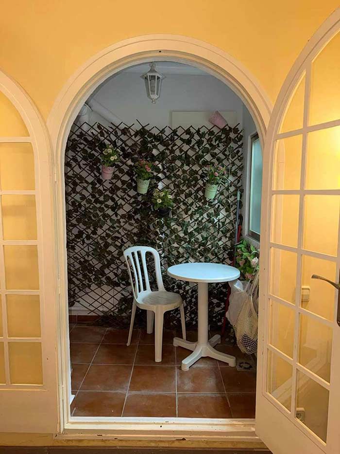 Pequeño patio con una silla blanca y una mesa redonda, visible a través de unas puertas francesas arqueadas abiertas.