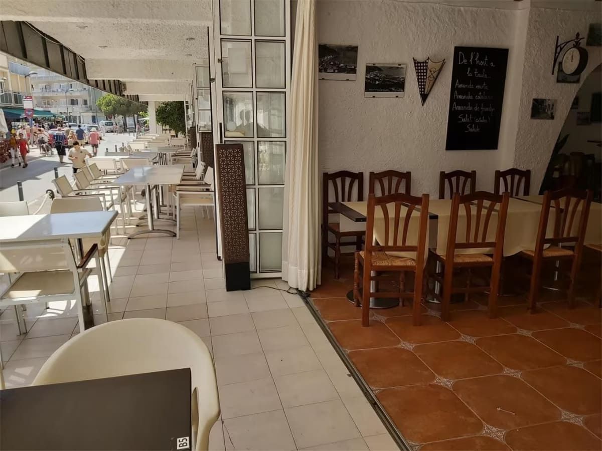 Interior de restaurante con mesas interiores y asientos en la acera con vista a una calle con peatones.