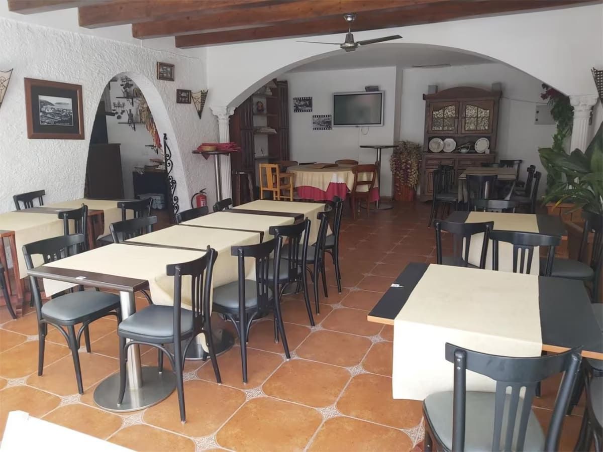 Interior de restaurante con mesas, sillas, puertas arqueadas y un mueble decorativo.
