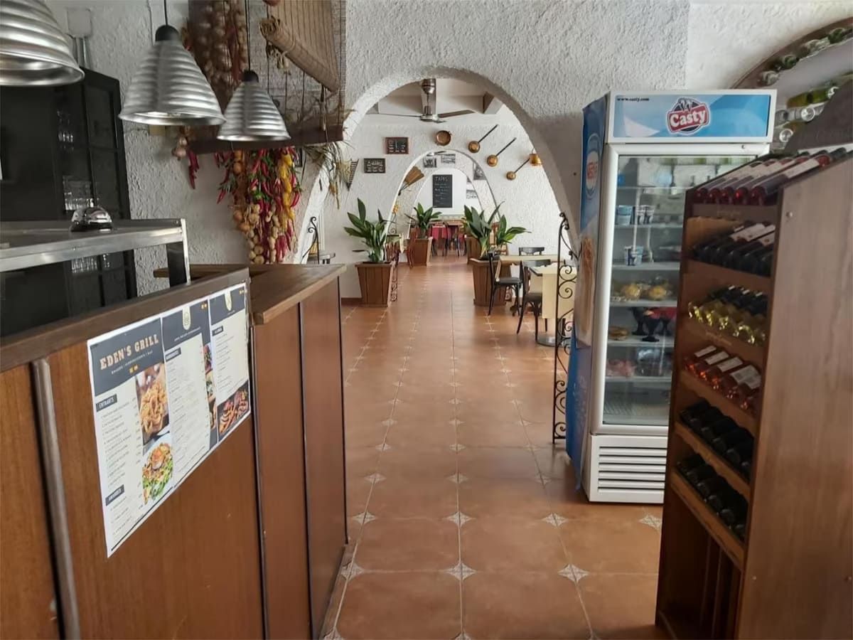 Interior de un restaurante con puertas arqueadas, mesas y un refrigerador visible.