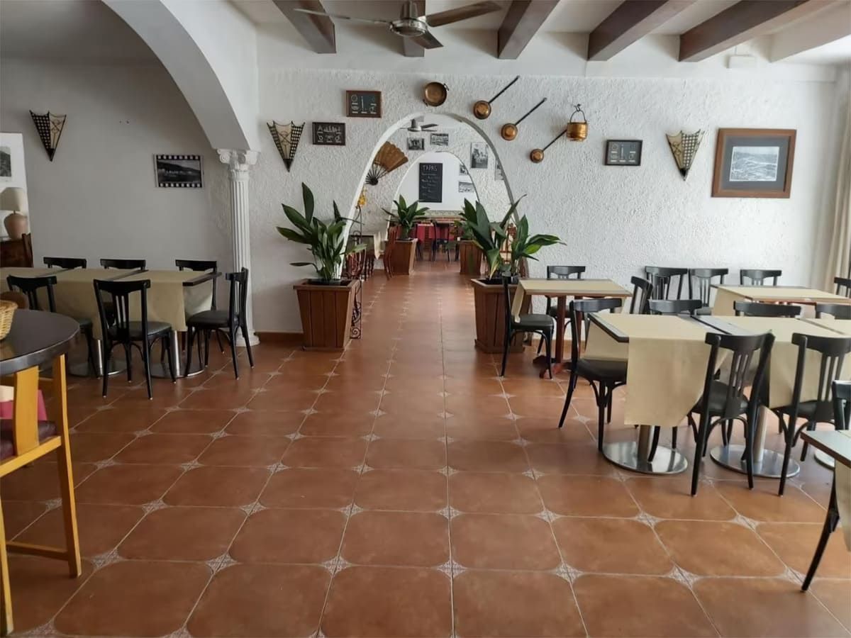 Interior de restaurante con mesas y sillas, arco, plantas y arte mural decorativo.