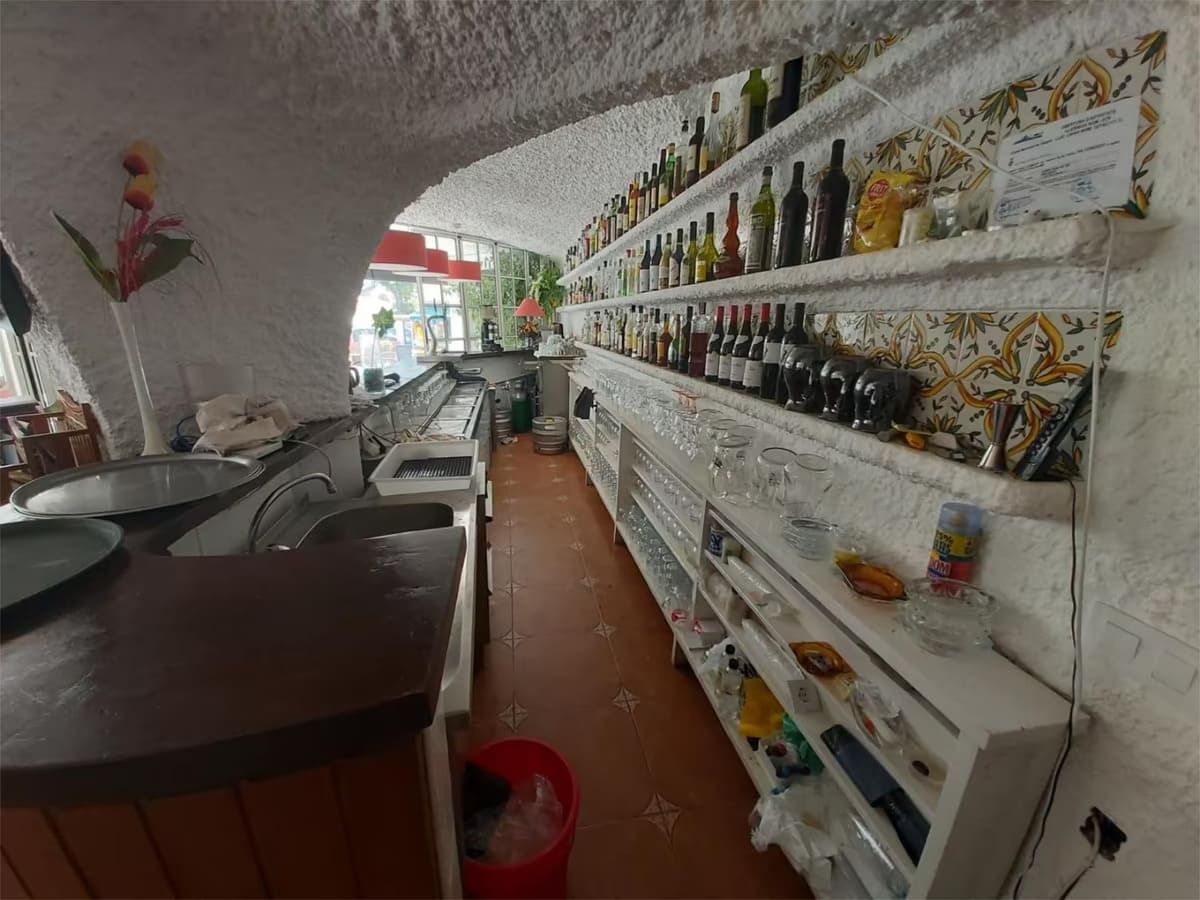 Interior de un pequeño restaurante con techo blanco curvo, barra y estantes de botellas; suelo rojo.
