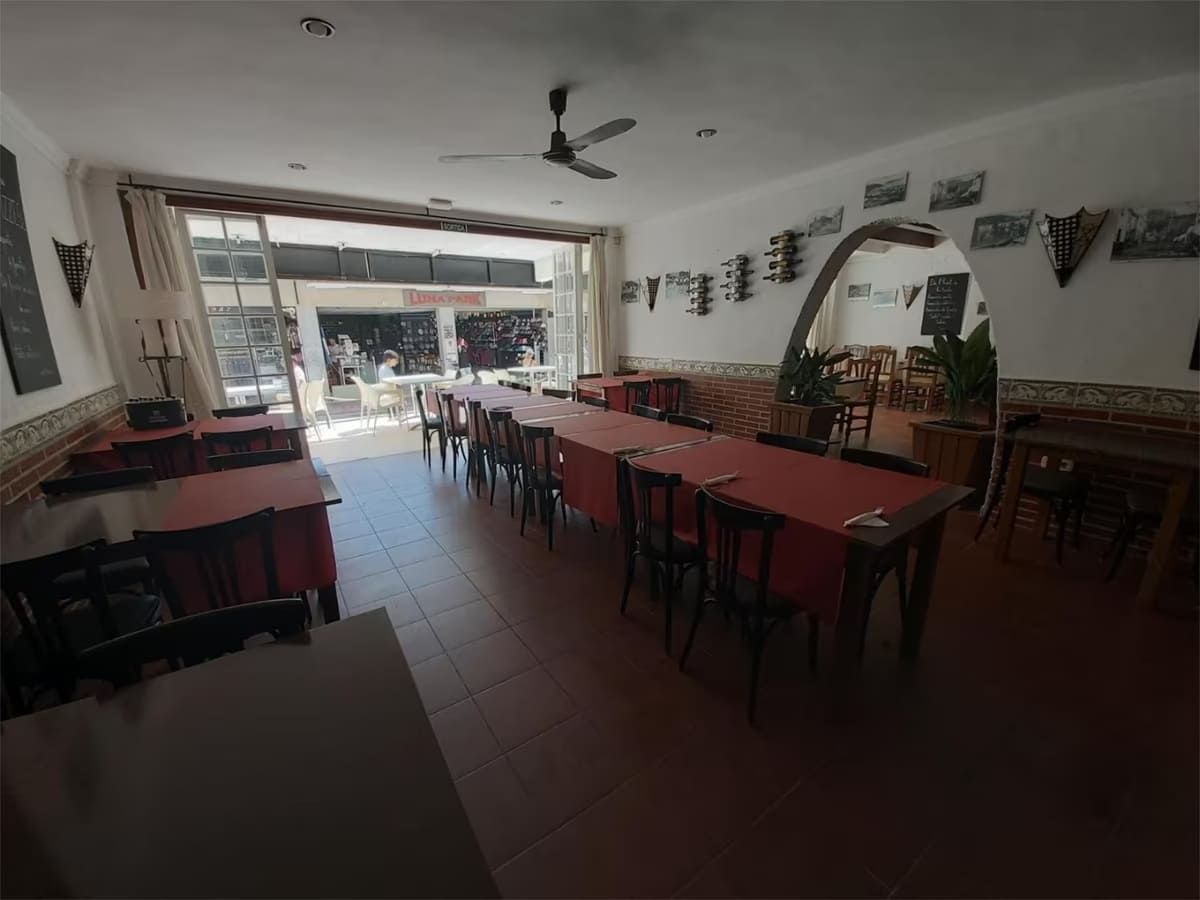 Interior de un restaurante con mesas, sillas y puerta abierta al exterior.