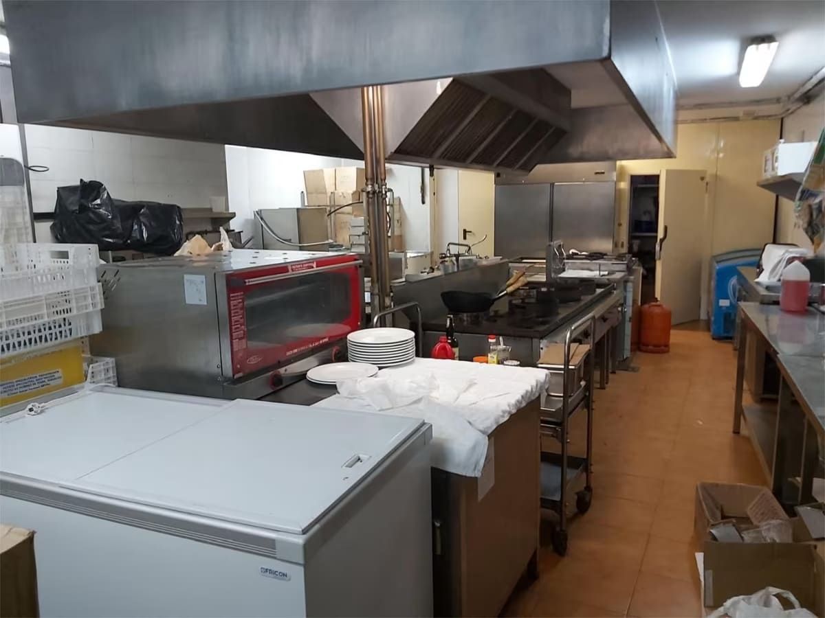 Cocina comercial con electrodomésticos de acero inoxidable, estufa, horno y campana extractora.