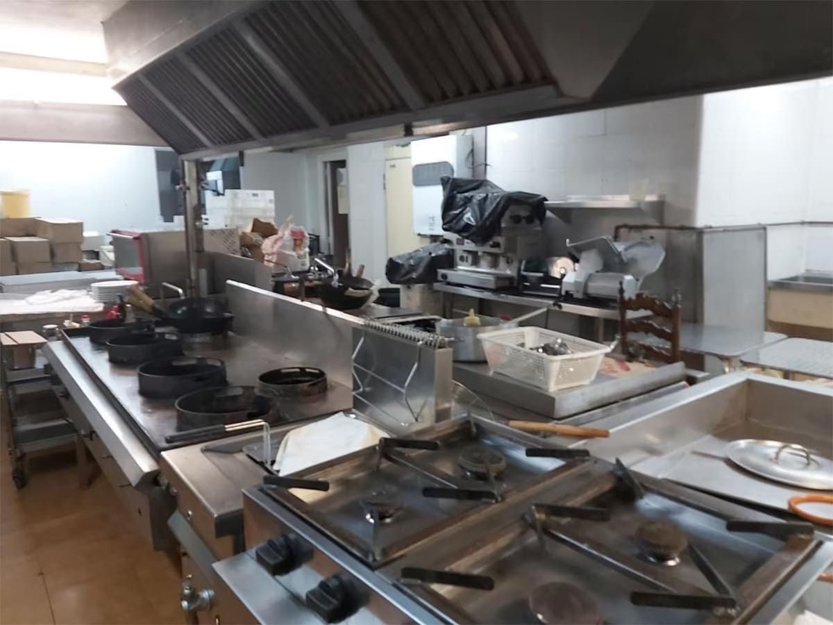 Cocina comercial con electrodomésticos de acero inoxidable, incluidas estufas y campana extractora.