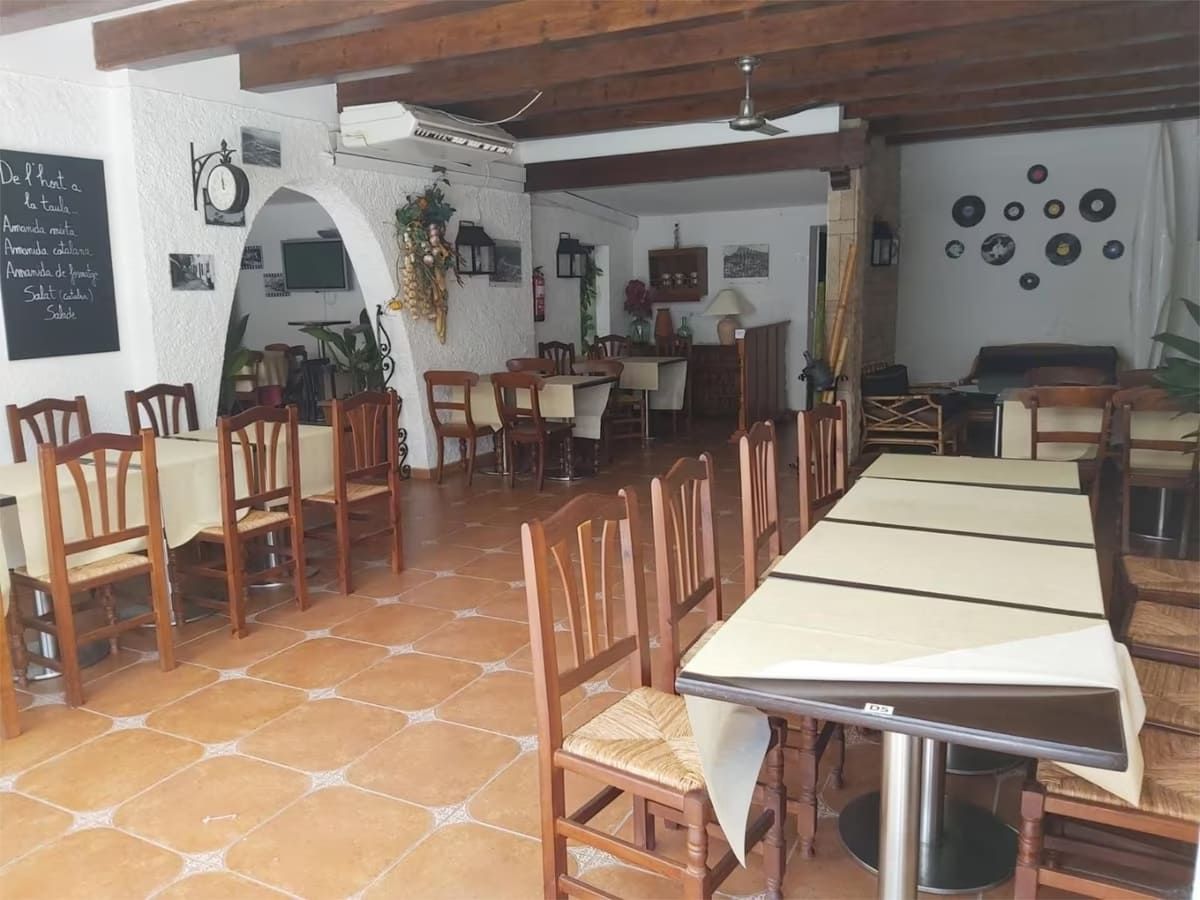 Interior de restaurante con mesas, sillas y decoraciones en las paredes. Mesas beige, sillas de madera y suelo de baldosas.