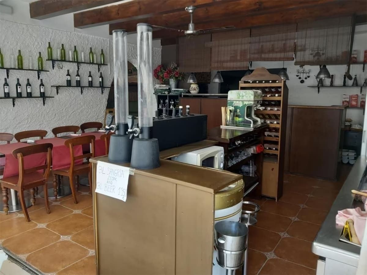 Interior de un restaurante con bar, asientos, botellas de vino en estantes y un ventilador de techo.