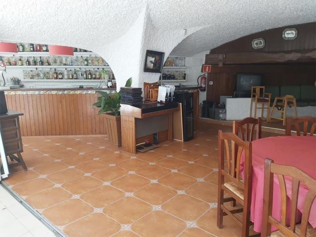 Interior de un restaurante con barra, mesas y sillas. Suelo de baldosas naranjas, techo blanco y una barra bien surtida.