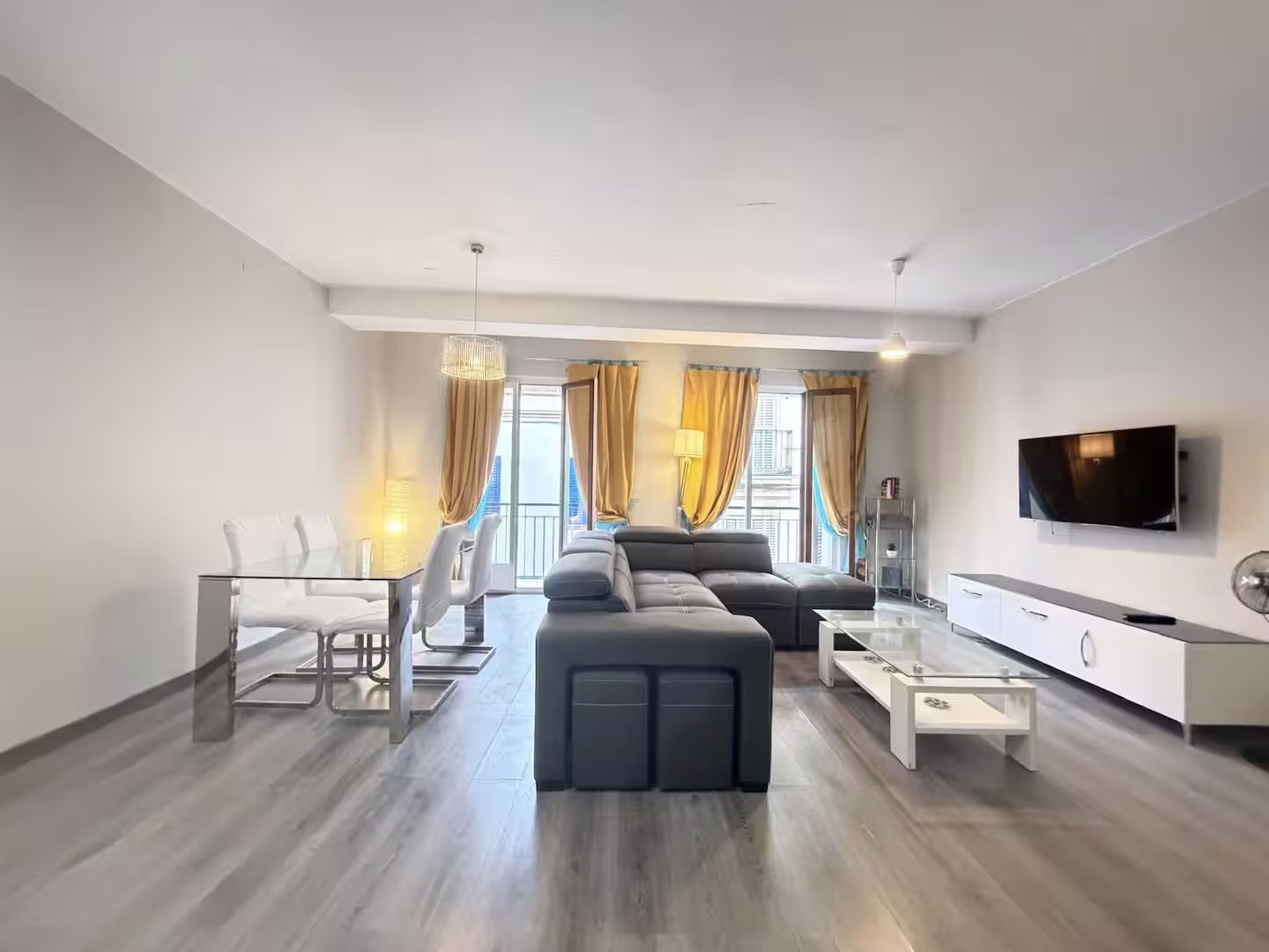 Sala de estar moderna con sofá modular gris, mueble de televisión blanco y cortinas amarillas junto a una gran ventana.