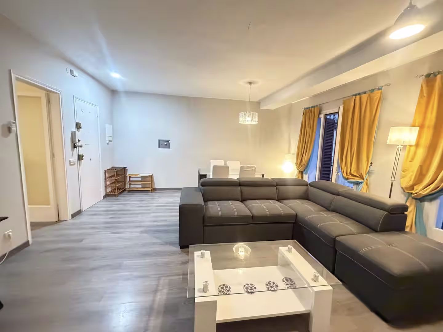 Sala de estar luminosa con sofá modular oscuro, mesa de centro blanca y cortinas doradas junto a la ventana.