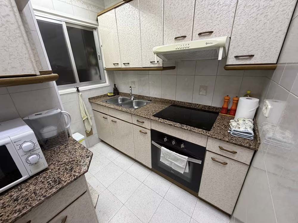 Cocina compacta de color beige con estufa, horno, fregadero, ventana y electrodomésticos de encimera.