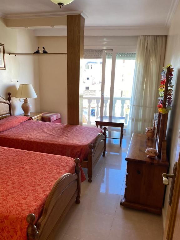 Habitación de hotel con dos camas individuales, muebles de madera y balcón con vistas a través de puertas de cristal.