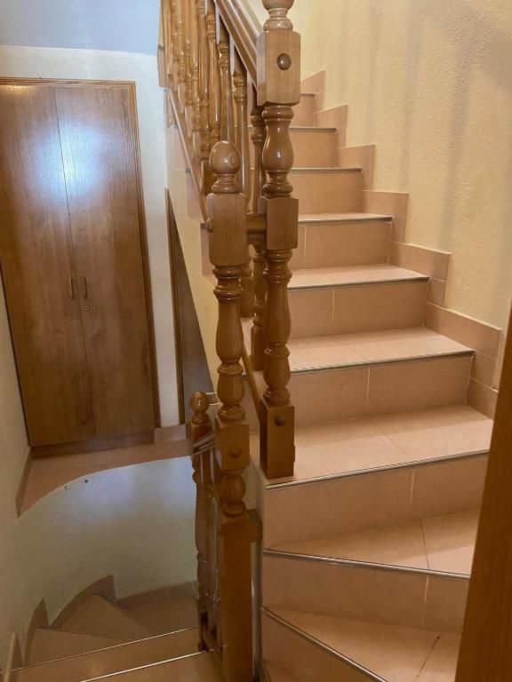 Escalera de madera con alfombra beige y barandilla ornamentada junto a una puerta del pasillo.