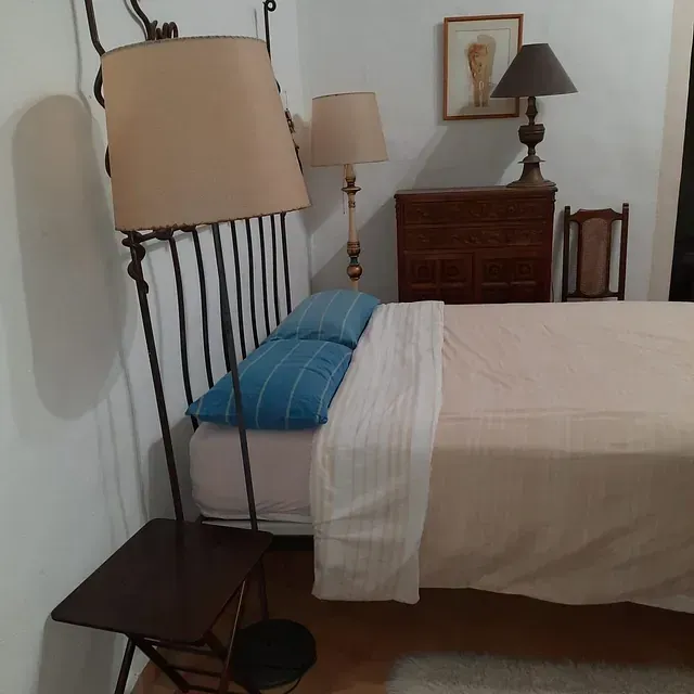 Un dormitorio con una cama, una lámpara y una silla.