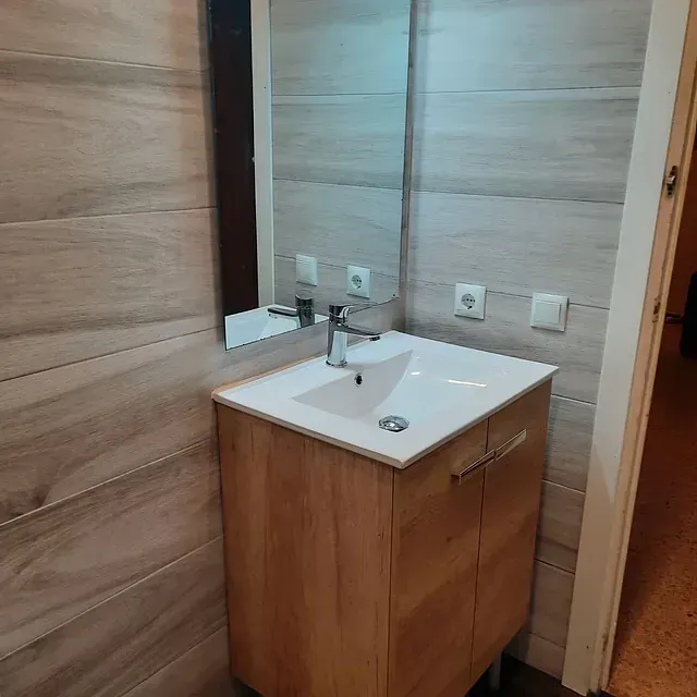 Un baño con lavabo, espejo y mueble de madera.