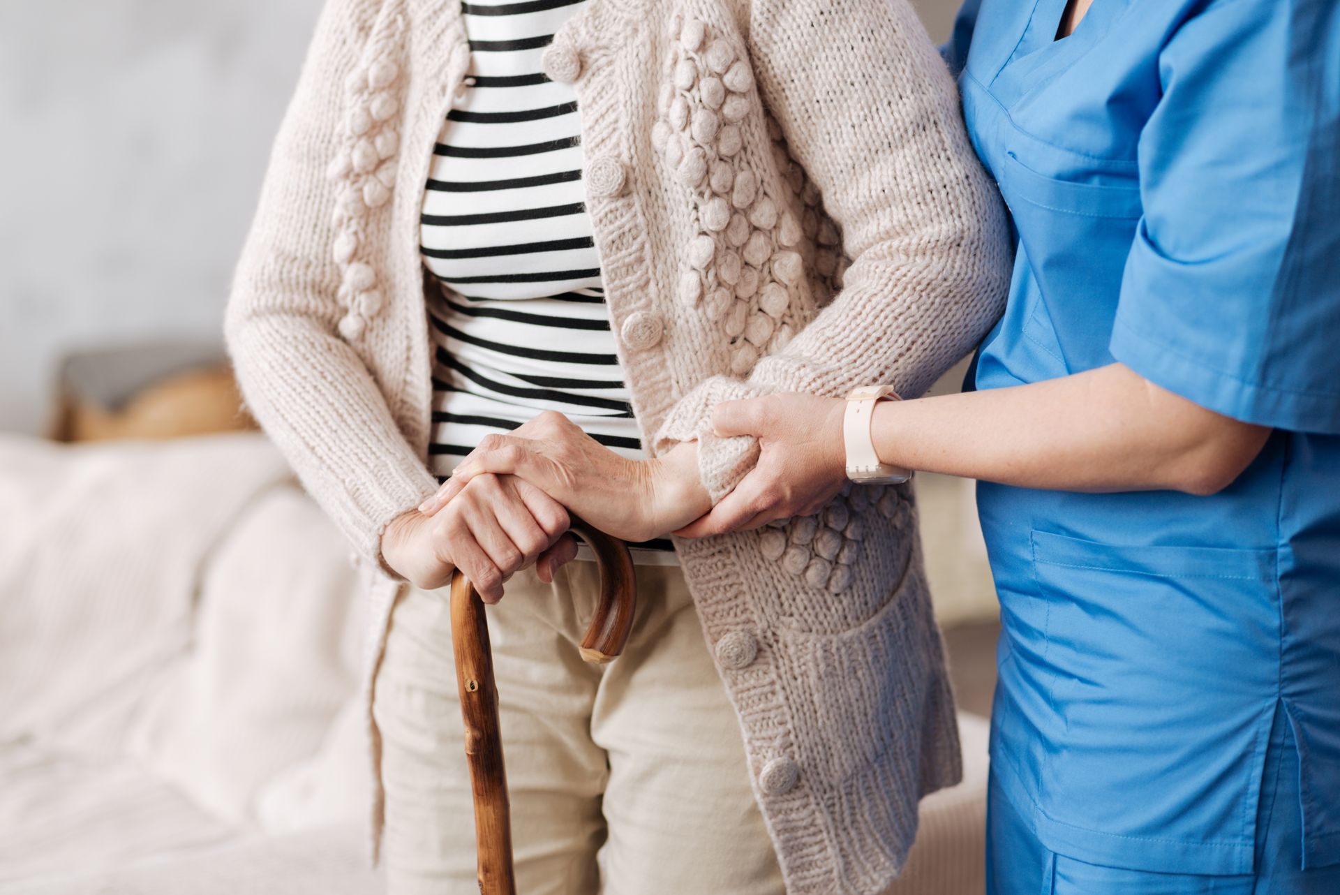 Une soignante soutient un patient muni d'une canne, en lui tenant la main dans un cadre domestique lumineux