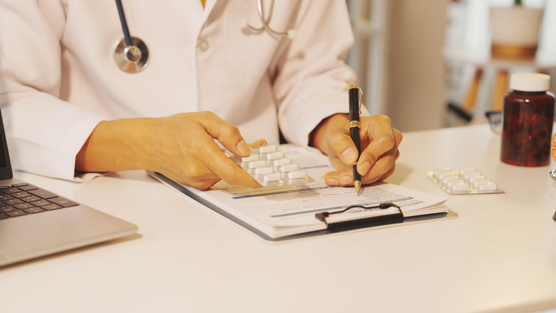 Un médecin prend des notes sur un bloc-notes à son bureau, un ordinateur portable et un flacon de médicament à proximité.
