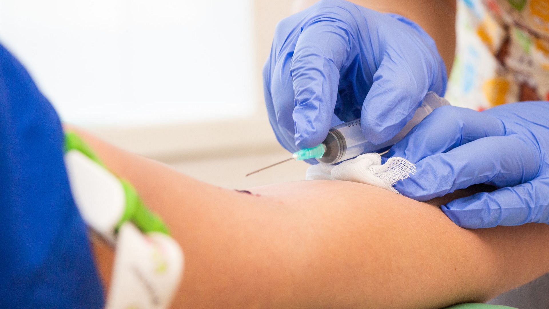 Des mains gantées administrent une injection dans un bras à l'aide d'un coton-tige tenu à proximité.