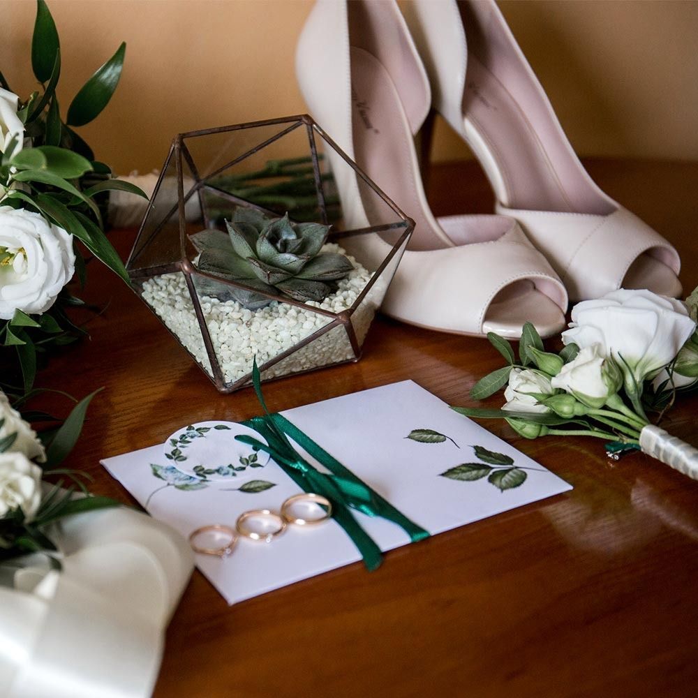 Una mesa con un ramo de flores, zapatos, anillos y un terrario.