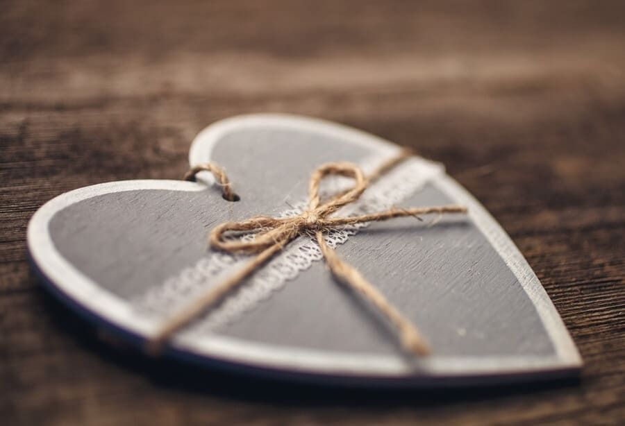 Un corazón de madera con una cuerda atada a su alrededor está sobre una mesa de madera.