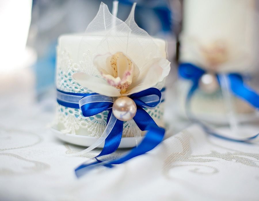 Una vela blanca decorada con una cinta azul y una perla sobre una mesa.