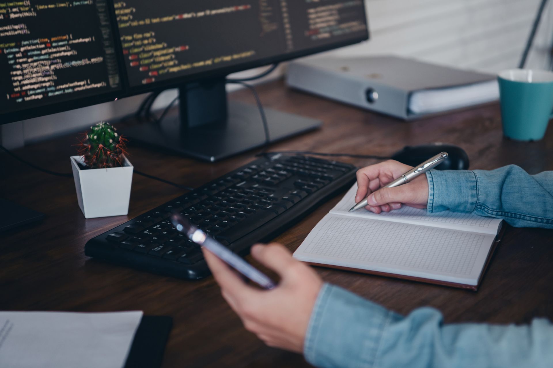 Una persona está escribiendo en un cuaderno mientras sostiene un teléfono celular.