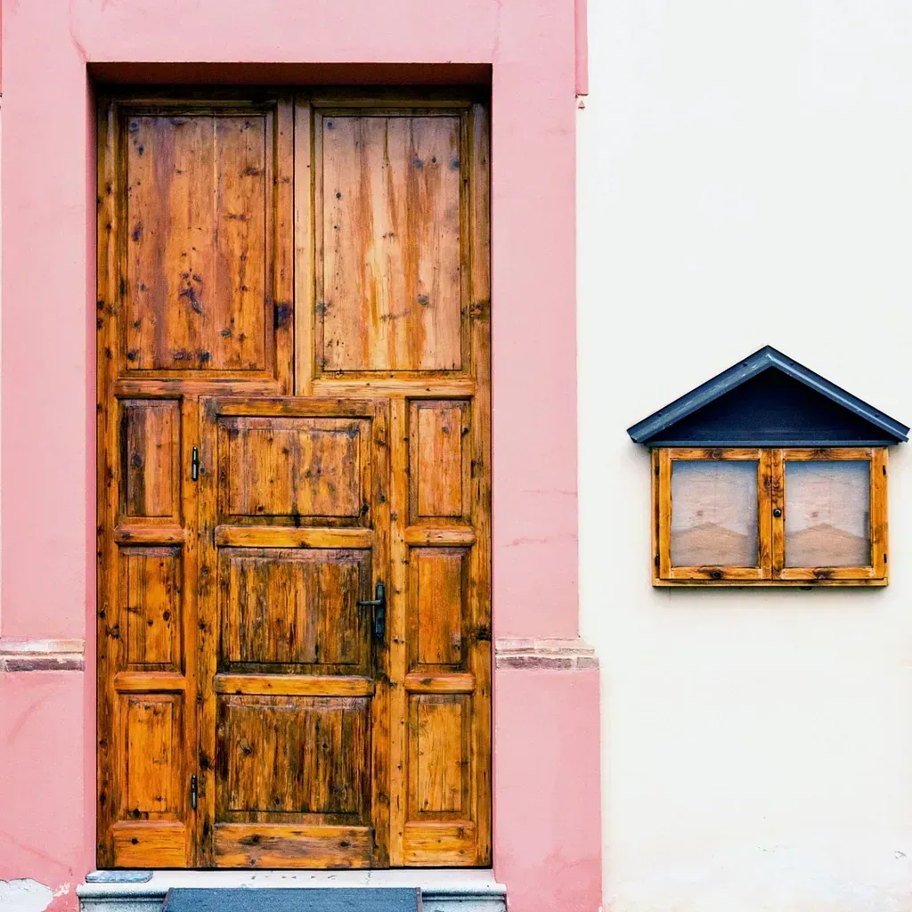 Una puerta de madera está en un edificio rosa y blanco al lado de un buzón.