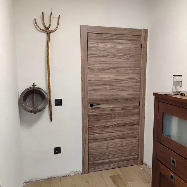 Una habitación con una puerta de madera y un tridente en la pared.