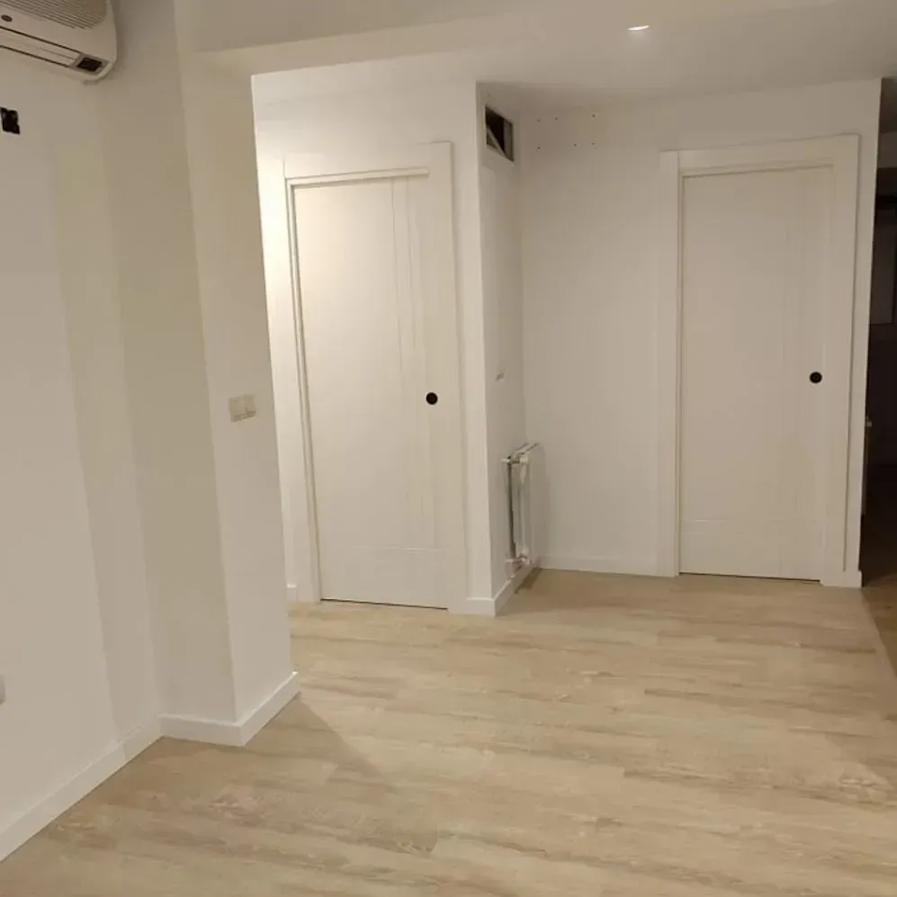 Una habitación vacía con suelo de madera y paredes blancas.